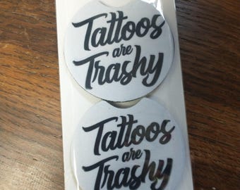 Puede incluir: Dos posavasos para coche con el texto "Tattoos are Trashy" en escritura negra sobre fondo blanco. Los posavasos están empaquetados juntos y etiquetados "Car Coasters" y "Handmade with love".
