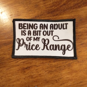 Könnte beinhalten: Weißer Patch mit schwarzem Rand und braunem Text, der "Erwachsen sein ist ein bisschen zu teuer" lautet.