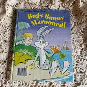 May include: A vintage "Little Golden Book" titled "Bugs Bunny Marooned!" features Bugs Bunny holding a carrot on a tropical island. The cover is blue with yellow and white text, and illustrations of a boy, palm trees, and a ship.