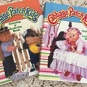 May include: Two vintage Cabbage Patch Kids coloring and activity books. One book has an orange cover with a cartoon boy holding a rake. The other book has a blue cover with a cartoon girl in curlers. Both books have the Cabbage Patch Kids logo.