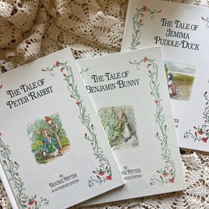 May include: Three vintage children's books with white covers and floral borders. The titles are "The Tale of Peter Rabbit," "The Tale of Benjamin Bunny," and "The Tale of Jemima Puddle-Duck." Each book features illustrations and the author's name, Beatrix Potter.