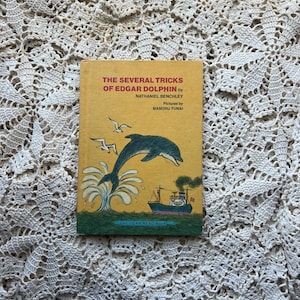 May include: A vintage children's book titled "The Several Tricks of Edgar Dolphin" by Nathaniel Benchley, with illustrations by Mamoru Funai. The cover features a dolphin leaping from the water, a ship, and the text "An I Can Read Book."