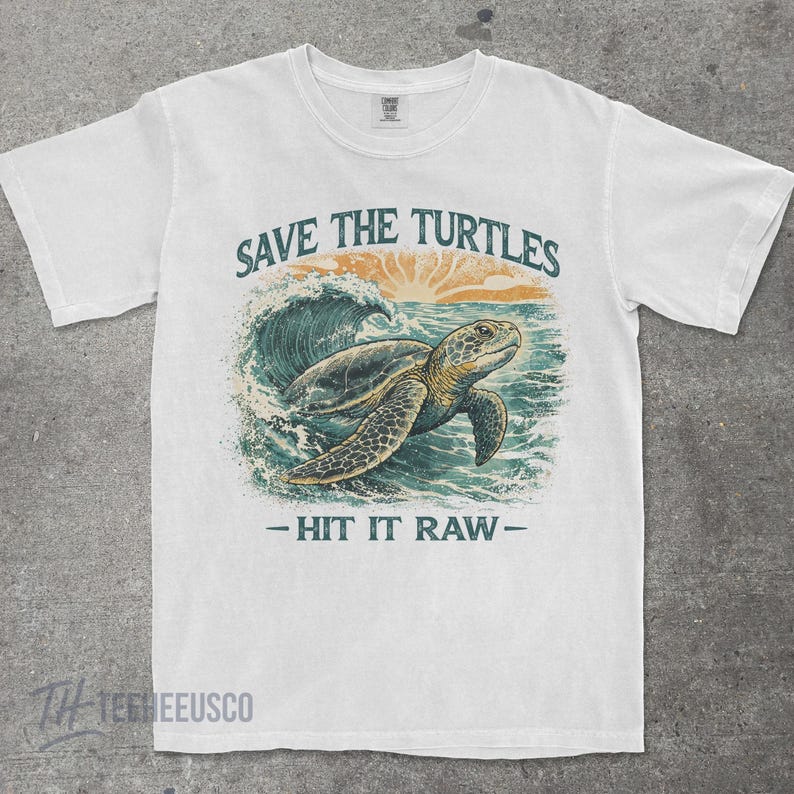 May include: White t-shirt with a graphic of a sea turtle swimming in the ocean. The text "SAVE THE TURTLES" is above the turtle, and "- HIT IT RAW -" is below. The design features shades of blue, green, and orange.