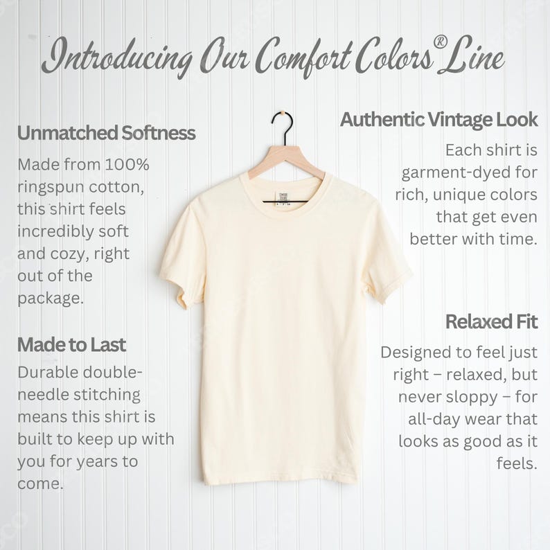 May include: Cream-colored Comfort Colors t-shirt hanging on a wooden hanger. The shirt is displayed against a white background with text that reads "Introducing Our Comfort Colors Line". The shirt is made of ringspun cotton.