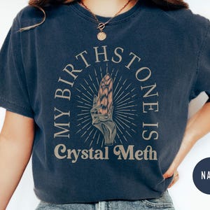 May include: A navy blue t-shirt with a graphic of a hand holding a crystal. The text "My Birthstone Is Crystal Meth" is printed on the shirt.