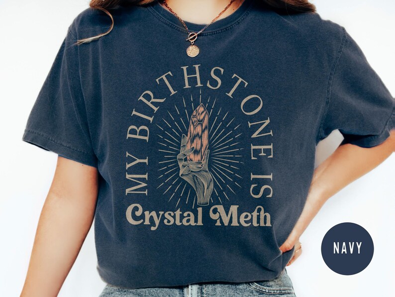 May include: A navy blue t-shirt with a graphic of a hand holding a crystal. The text "My Birthstone Is Crystal Meth" is printed on the shirt.