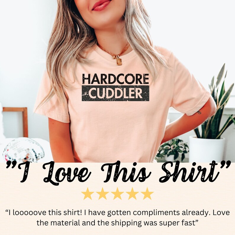 Puede incluir: Una camiseta rosa con el texto "HARDCORE CUDDLER" en negro con un efecto desgastado. La camiseta la lleva puesta una persona. El texto "Me encanta esta camiseta" est&aacute; debajo de la imagen con cinco estrellas doradas.