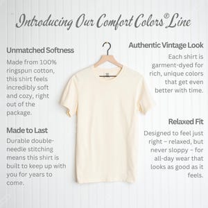 May include: Cream-colored t-shirt hanging on a wooden hanger. The shirt is part of the "Comfort Colors" line and is made of ringspun cotton. Text on the left describes the shirt's softness and durability. Text on the right describes the vintage look and relaxed fit.