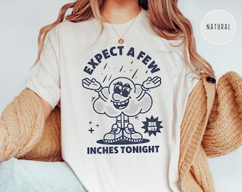 Puede incluir: Una camiseta blanca con un gráfico de nube de dibujos animados y el texto "Expect a few big wet inches tonight".
