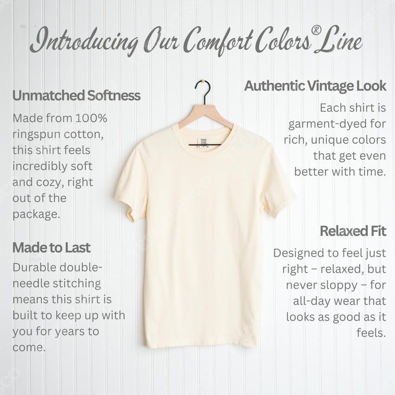 May include: A cream-colored t-shirt hangs on a wooden hanger. The text "Introducing Our Comfort Colors Line" is at the top. The shirt is described as having unmatched softness, an authentic vintage look, and a relaxed fit.