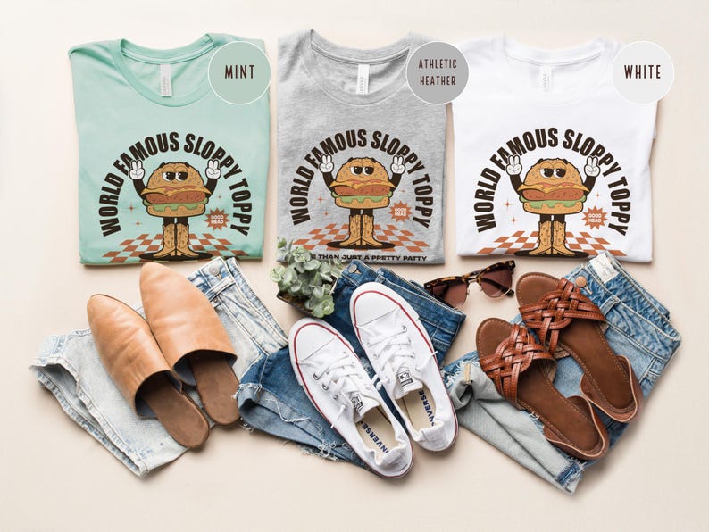 May include: Three t-shirts featuring a vintage cartoon burger design. The shirts are in mint, heather grey, and white. The text on the shirts reads "World Famous Sloppy Toppy".
