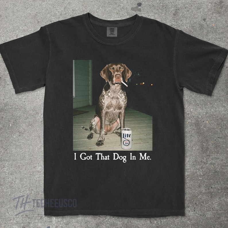 K&ouml;nnte beinhalten: Schwarzes T-Shirt mit einem Deutsch Kurzhaar, der eine Zigarette raucht, neben einer Dose Lite-Bier. Der Text "I Got That Dog In Me" ist darunter gedruckt.