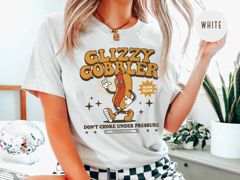 K&ouml;nnte beinhalten: Wei&szlig;es T-Shirt mit Retro-Grafik. Das Design zeigt eine Cartoon-Hotdog-Figur mit dem Text "GLIZZY GOBBLER" in Orange und Braun sowie dem Satz "DON'T CHOKE UNDER PRESSURE".