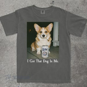 May include: Dark grey t-shirt with a graphic of a corgi dog smoking a cigarette and a Lite beer can. The text "I Got That Dog In Me" is printed below the image.