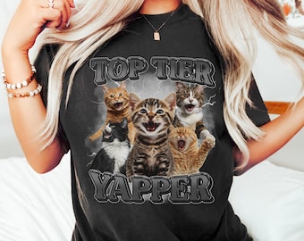 May include: Black t-shirt featuring a graphic of five cats with open mouths and the text "TOP TIER YAPPER" in a distressed font. The cats are in various colors, including orange, black, and tabby.