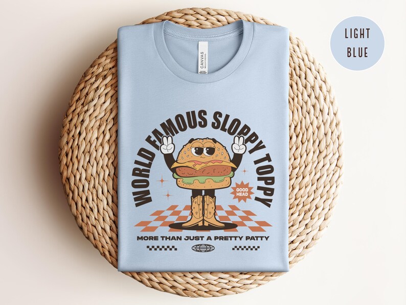 May include: Light blue t-shirt featuring a cartoon burger wearing cowboy boots and the text "World Famous Sloppy Toppy" and "More Than Just A Pretty Patty".
