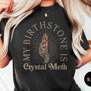 May include: Black t-shirt with a graphic of a hand holding a crystal with the text "My Birthstone Is Crystal Meth".