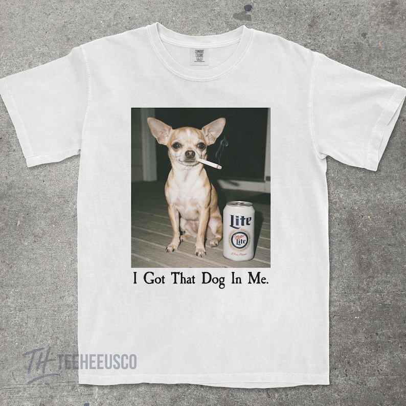 Puede incluir: Camiseta blanca con un gr&aacute;fico de un chihuahua con un cigarrillo en la boca y una lata de cerveza Lite. El texto "I Got That Dog In Me" est&aacute; impreso debajo de la imagen.