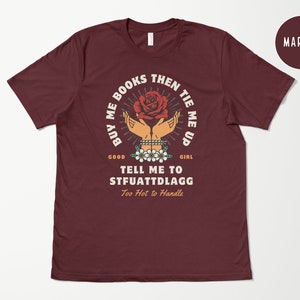 K&ouml;nnte beinhalten: Maroonfarbenes T-Shirt mit einem Motiv einer Hand, die eine rote Rose h&auml;lt, mit dem Text "BUY ME BOOKS THEN TIE ME UP GOOD GIRL TELL ME TO STFUATTDLAGG Too Hot to Handle"