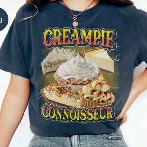 May include: A navy blue t-shirt with a graphic of various cream pies and the text "CREAMPIE CONNOISSEUR".