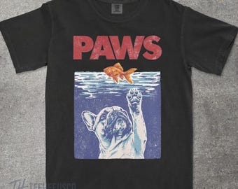 May include: Black t-shirt with a graphic design featuring the word "PAWS" in red above an illustration of a French Bulldog reaching for a goldfish. The design has a vintage, distressed look.