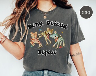May include: A gray t-shirt with the text "Deny. Defend. Depose." and a graphic of three cartoon deer. The deer are wearing floral headbands and are in a playful pose.