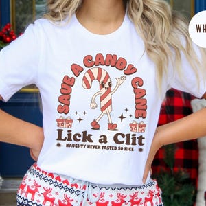 May include: White t-shirt with a red and white candy cane graphic and the text "Save a Candy Cane Lick a Clit Naughty Never Tasted So Nice".