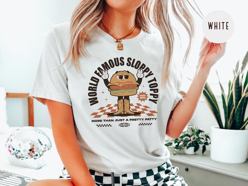 May include: White t-shirt featuring a cartoon burger graphic with the text "World Famous Sloppy Toppy" and "More Than Just A Pretty Patty".