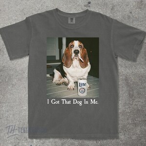 May include: Gray t-shirt featuring a graphic of a Basset Hound with a cigarette in its mouth, next to a can of Lite beer. The text "I Got That Dog In Me" is printed below the image.