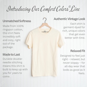 Puede incluir: Una camiseta color crema cuelga de una percha de madera. La camiseta forma parte de la l&iacute;nea Comfort Colors, con texto que describe su suavidad, durabilidad y aspecto vintage. La camiseta est&aacute; dise&ntilde;ada para un ajuste relajado.
