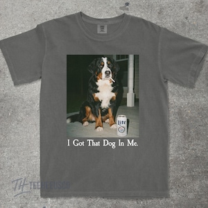 May include: Gray t-shirt featuring a graphic of a Bernese Mountain Dog with a cigarette in its mouth and a can of Lite beer. The text "I Got That Dog In Me" is printed below the image.