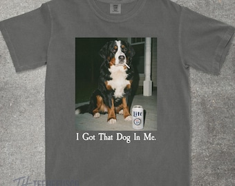 May include: Gray t-shirt featuring a graphic of a Bernese Mountain Dog with a cigarette in its mouth and a can of Lite beer. The text "I Got That Dog In Me" is printed below the image.