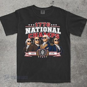 May include: Black t-shirt featuring a graphic with the text "1776 NATIONAL CHAMPS" above an illustration of four historical figures wearing sunglasses. The design includes stars, a banner, and the text "EST. 1776".