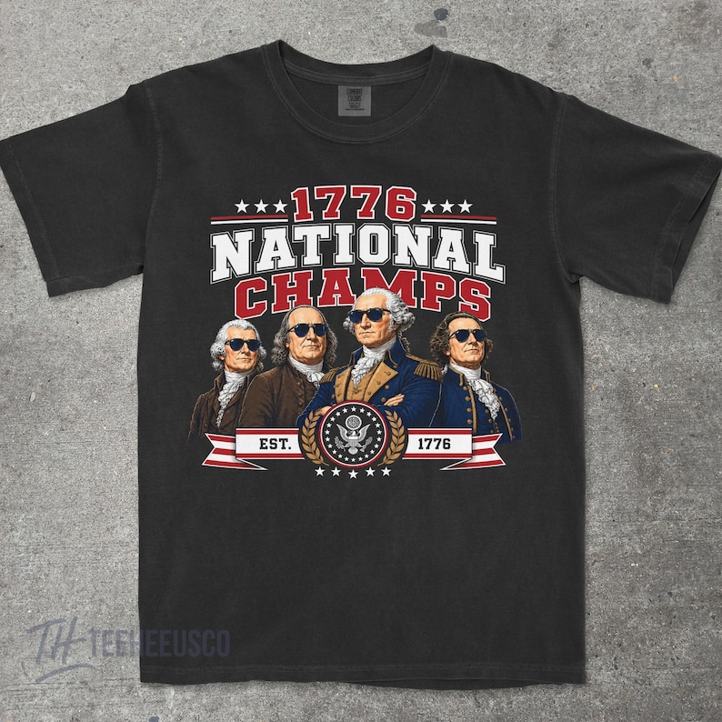 May include: Black t-shirt featuring a graphic with the text "1776 NATIONAL CHAMPS" above an illustration of four historical figures wearing sunglasses. The design includes stars, a banner, and the text "EST. 1776".