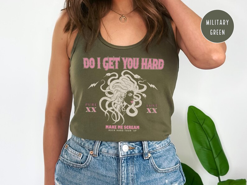 May include: An olive green vest top with the pink text "DO I GET YOU HARD". The graphic features a Medusa illustration with the words "PURE XX" and "LUST XX". The text "MAKE ME SCREAM ROCK HARD TOUR 69" is also present.