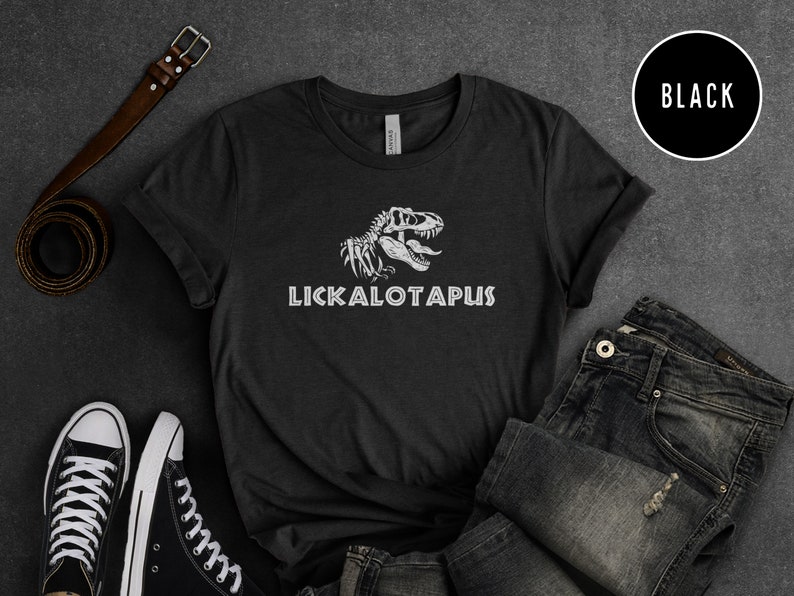 Może przedstawiać: Czarny T-shirt z białym nadrukiem szkieletu dinozaura i tekstem "LICKALOTAPUS".