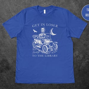 May include: A royal blue t-shirt with a white graphic of a man driving a vintage car with the text "Get in loser, we're going to the library".