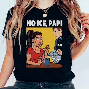 May include: Black t-shirt with a comic-style illustration. The image features a woman gesturing in protest as a man pours ice into a cup. Text above reads "NO ICE, PAPI."