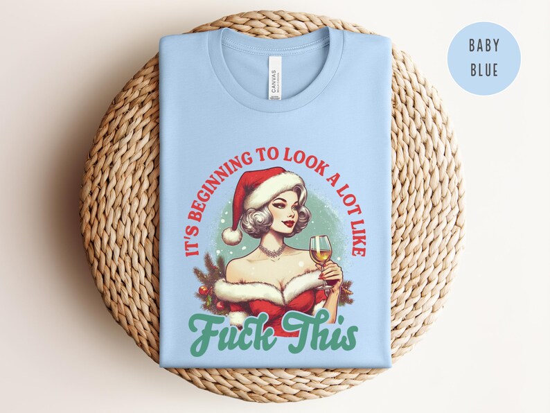 Pu&ograve; includere: T-shirt azzurra con una grafica di una donna con un cappello di Babbo Natale che tiene in mano un bicchiere di vino. Il testo sulla maglietta recita "It's beginning to look a lot like Fuck This."