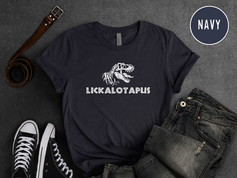 Może przedstawiać: Koszulka w kolorze granatowym z białym nadrukiem szkieletu dinozaura i tekstem "LICKALOTAPUS".