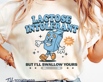 Puede incluir: Camiseta color crema con las palabras "LACTOSE INTOLERANT" en azul, con un personaje de cartón de leche de dibujos animados. El texto "BUT I'LL SWALLOW YOURS" está debajo del dibujo animado. La camiseta también tiene el texto "GOT CREAM?" y la marca "TEEHEEUSCO".