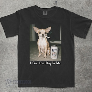 Puede incluir: Camiseta negra con un dise&ntilde;o gr&aacute;fico humor&iacute;stico. Muestra un perro peque&ntilde;o con un cigarrillo en la boca y una lata de cerveza Lite. El texto "I Got That Dog In Me" est&aacute; debajo de la imagen.