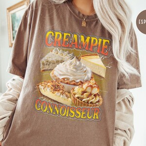 May include: Brown t-shirt with a graphic of various pies and the text "CREAMPIE CONNOISSEUR".