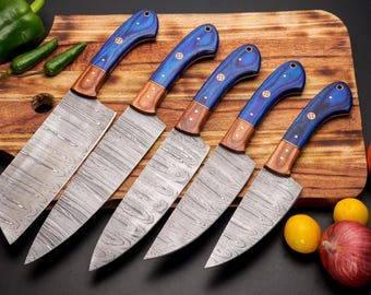May include: Set of six kitchen knives with blue and brown handles. The knives have a Damascus steel blade and are arranged on a wooden cutting board.