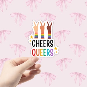 May include: A sticker with three hands in a peace sign, each with a different skin tone, wearing rainbow bracelets. The text "*CHEERS QUEERS*" is below the hands.
