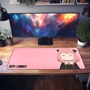 May include: Pink anime-style mouse mat featuring a character from the show "SPY×FAMILY" on the right side. The character has pink hair and is wearing a black and white outfit. The text "SPY×FAMILY" is printed in black on the left side of the mouse mat.
