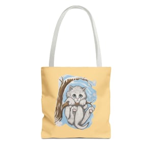 Peut inclure: Sac fourre-tout jaune clair avec une poignée blanche. Le sac présente une illustration de dessin animé d'un chaton gris suspendu à une branche d'arbre. Le chaton a les yeux bleus et les pattes roses, avec des flocons de neige en arrière-plan.