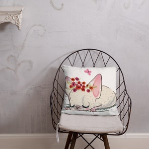 May include: A white throw pillow with a cartoon illustration of a sleeping dog wearing a flower crown. The dog has pink ears and a pink butterfly is flying above it.