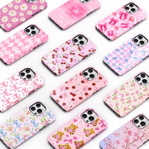 May include: A collection of 12 different phone cases with various cute and colorful patterns. The cases feature designs like cherries, bows, gingham, and floral prints. The cases are all pink and white.