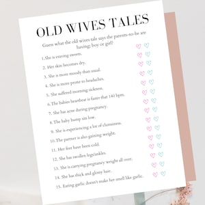 May include: A white card with the text "OLD WIVES TALES" and a list of pregnancy symptoms. The card includes pink and blue heart icons for a baby shower game. The card is on a pink background.